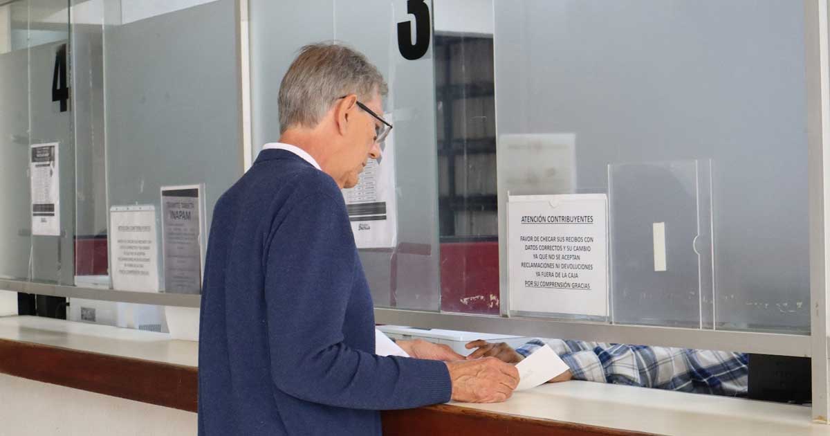 Adulto mayor pagando impuestos en ventanilla.