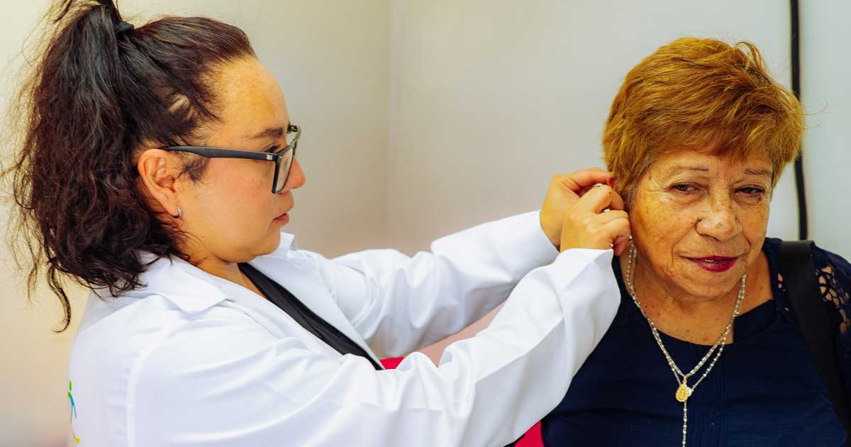 Doctora colocando un aparato auditivo a una mujer mayor.