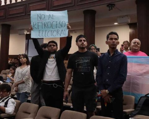 Integrantes de la comunidad LGBT sosteniendo una pancarta y levantando la bandera transgénero en el interior del Congreso de Coahuila.