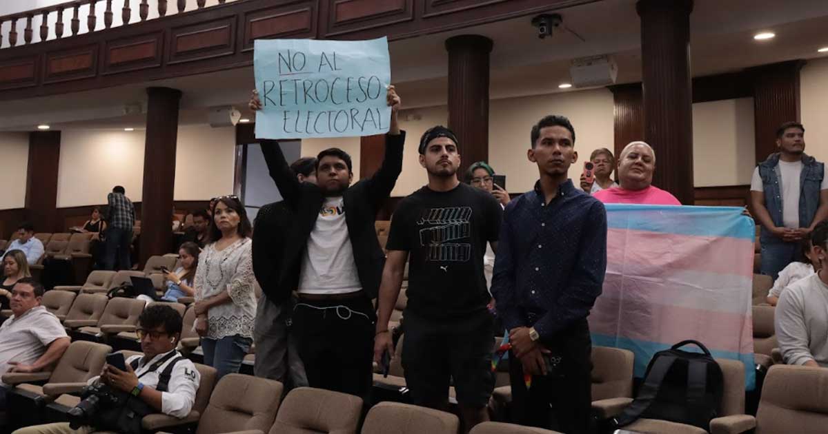 Integrantes de la comunidad LGBT sosteniendo una pancarta y levantando la bandera transgénero en el interior del Congreso de Coahuila.