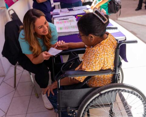 Luly López entregando apoyo económico a una mujer en silla de ruedas.