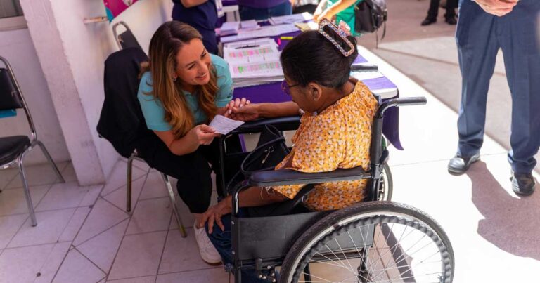 Luly López entregando apoyo económico a una mujer en silla de ruedas.