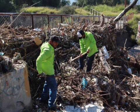Trabajadores retirando basura y escombro de puente peatonal.