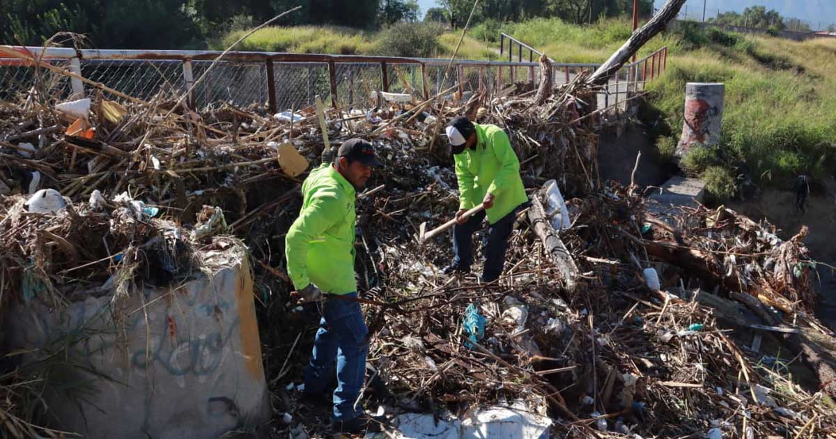 Trabajadores retirando basura y escombro de puente peatonal.