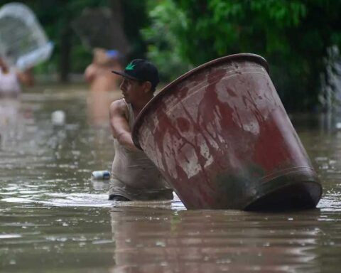 Un hombre, con el agua hasta la cintura, empujando una enorme tina por la calle.
