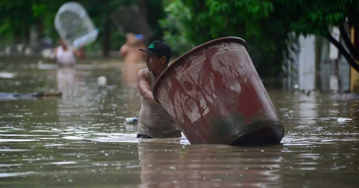 Un hombre, con el agua hasta la cintura, empujando una enorme tina por la calle.