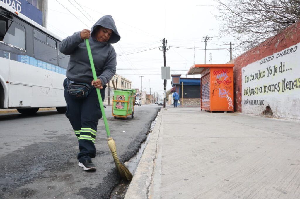 Mujer del programa Aquí Andamos barriendo una calle en Saltillo.