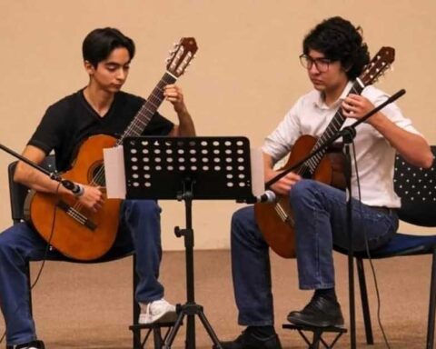 Dos jóvenes sentados tocando guitarra.