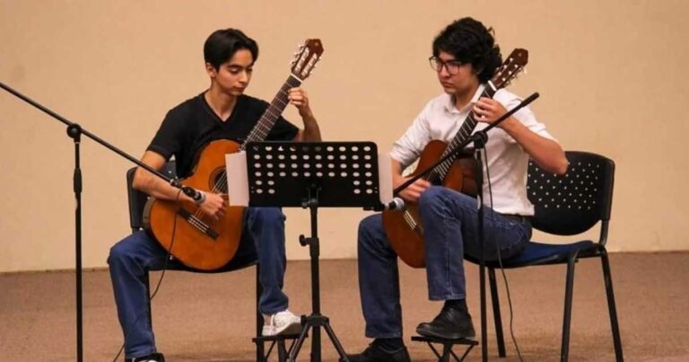 Dos jóvenes sentados tocando guitarra.