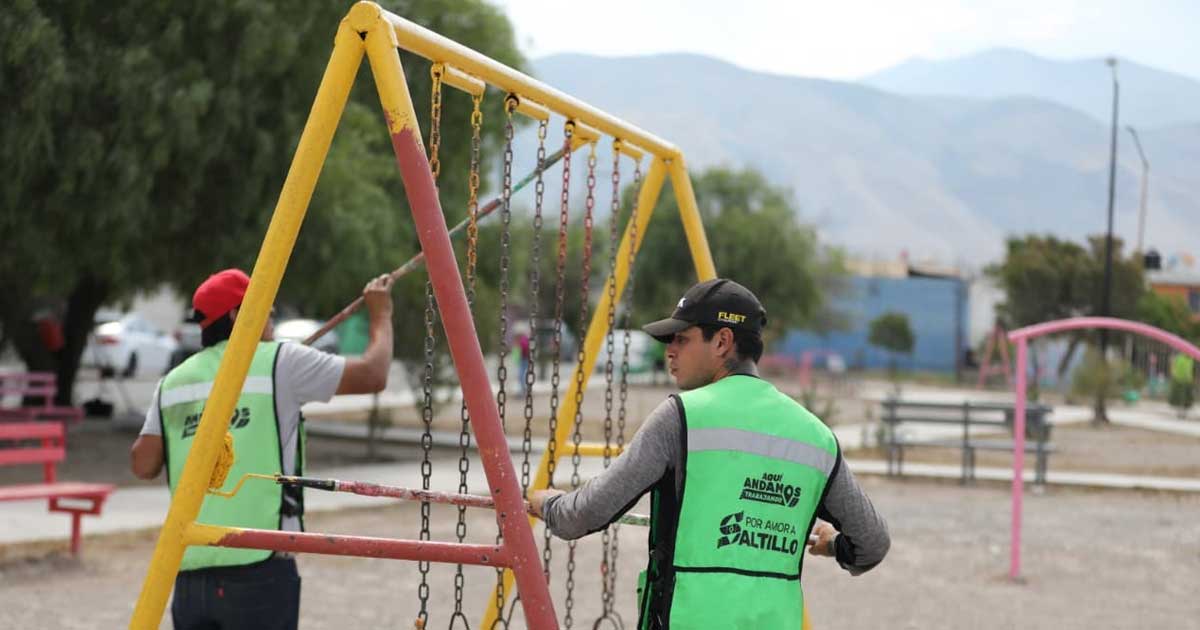 Trabajadores de Saltillo pintando columpios en plaza pública.
