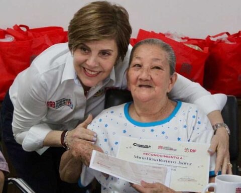 La presidenta del DIF Torreón abrazando y dando un reconocimiento en papel a una adulta mayor.