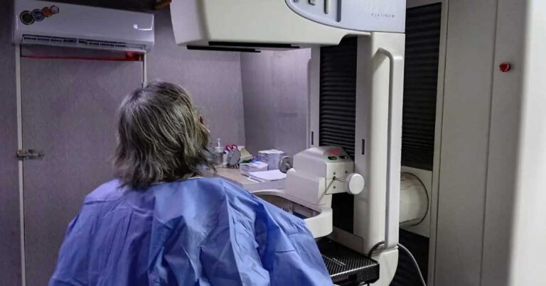 Una mujer de espaldas y frente a ella un mastógrafo.