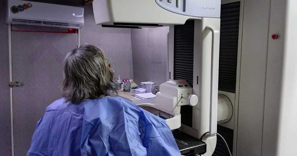 Una mujer de espaldas y frente a ella un mastógrafo.