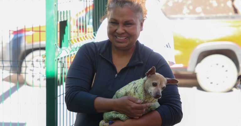 Una mujer cargando a un perro envuelto en una manta.
