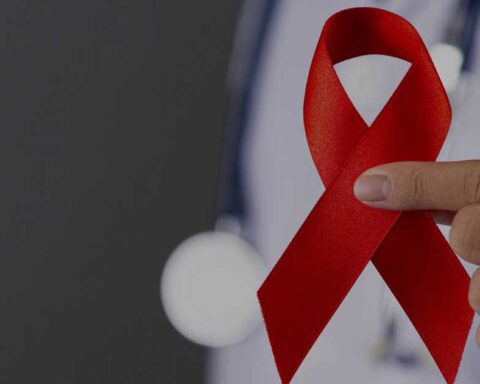 Una mujer con bata médica sosteniendo un lazo rojo.