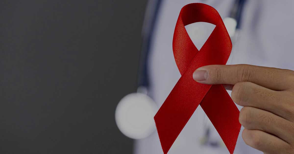 Una mujer con bata médica sosteniendo un lazo rojo.
