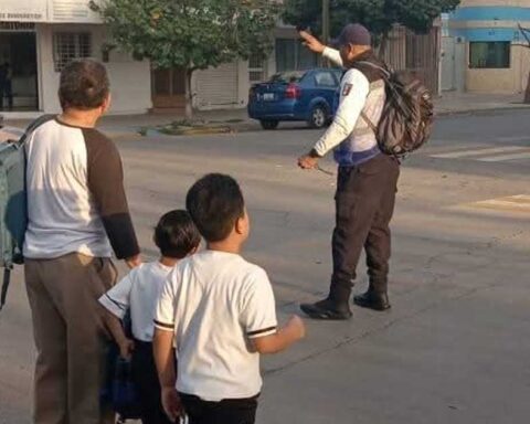 Niños y un hombre mayor atravesando una calle mientras un agente de Vialidad detiene la circulación en Torreón.