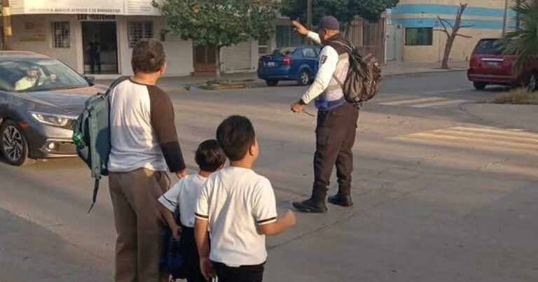 Niños y un hombre mayor atravesando una calle mientras un agente de Vialidad detiene la circulación en Torreón.