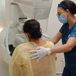 Enfermera guiando a una mujer de espaldas hacia el estudio de mastografía.