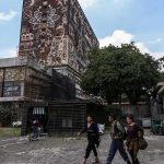 Jóvenes caminando frente al edificio principal de la UNAM.
