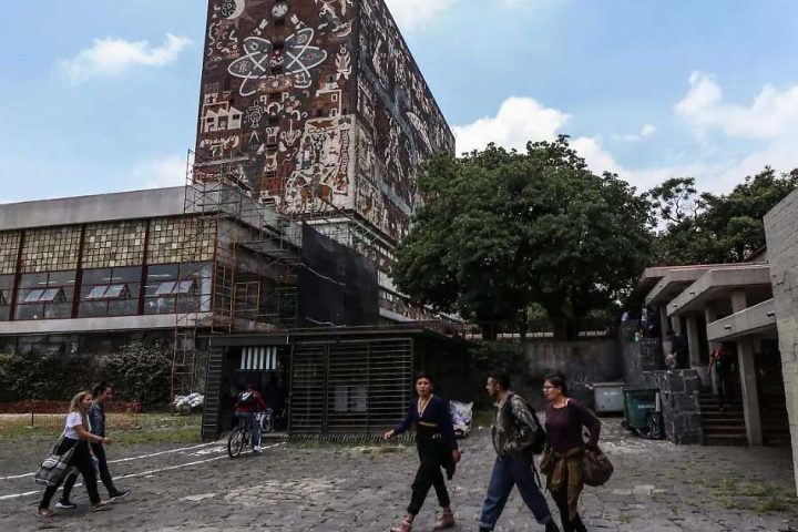 Jóvenes caminando frente al edificio principal de la UNAM.