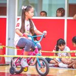 Una niña en una bicicleta; de fondo, más niñas.