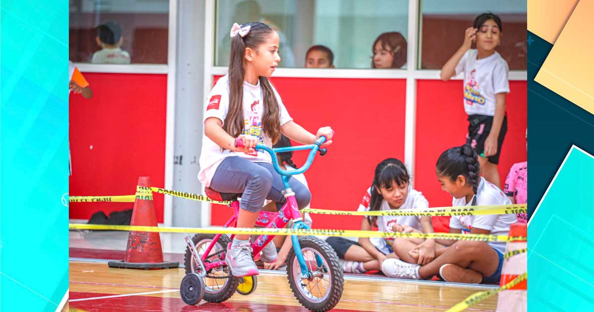 Una niña en una bicicleta; de fondo, más niñas.